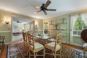 A dining area with a glass-top table surrounded by chairs, a ceiling fan, and a view of a garden through a window. - Historic BR Home | Walk to Main St | Pet Friendly (Blowing Rock)