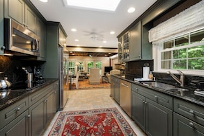 A modern kitchen with dark cabinetry, stainless steel appliances, and a large window. - Historic BR Home | Walk to Main St | Pet Friendly (Blowing Rock)