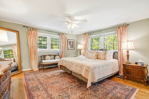 Een slaapkamer met een groot bed, een zitbankje, een dressoir en een plafondventilator.