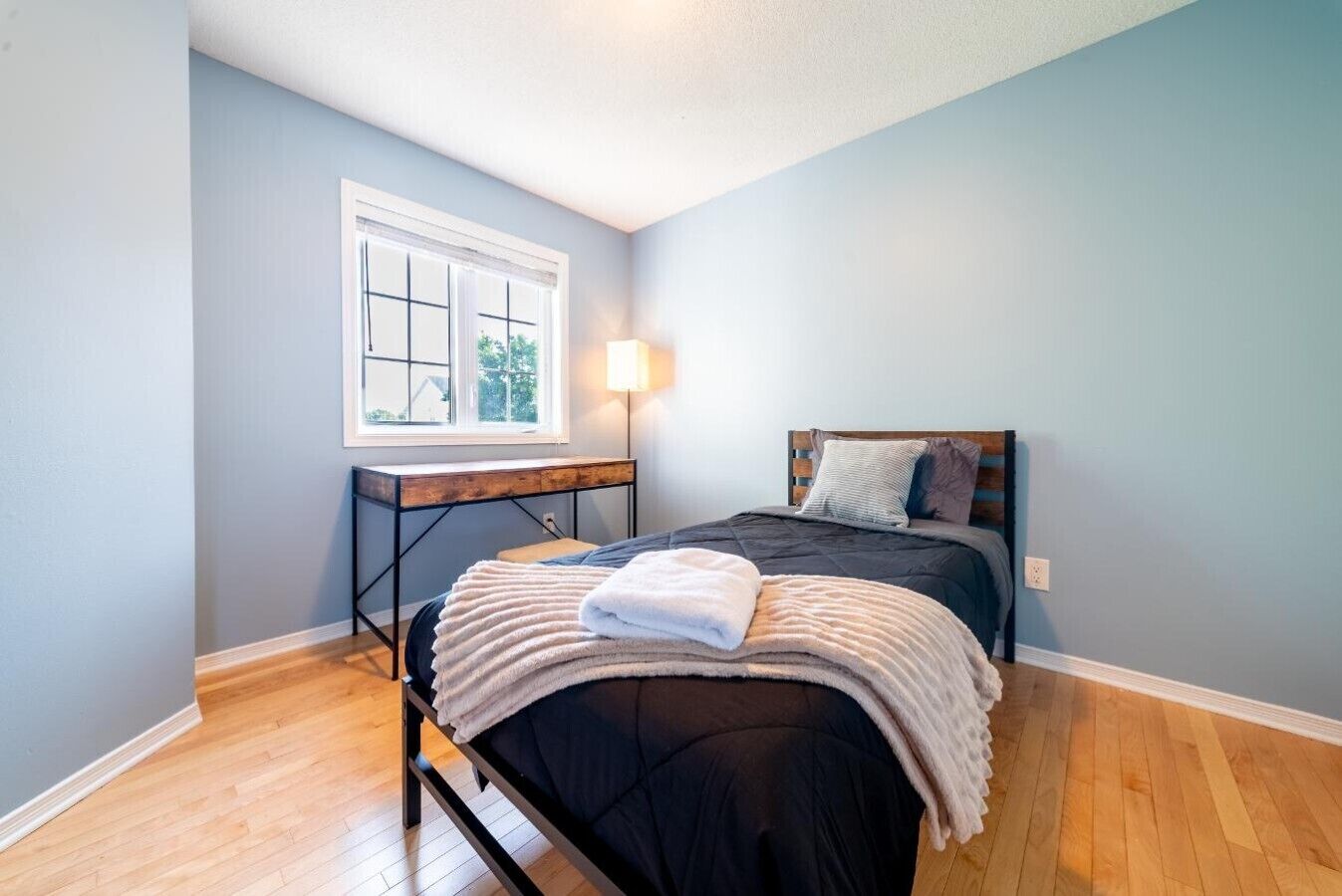 Une chambre à coucher avec un lit, un bureau, une lampe et une fenêtre.