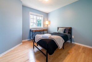 Een slaapkamer met een bed, nachtkastje, raam en lamp.