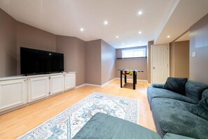 Een woonkamer met een flatscreen televisie, een tafelvoetbaltafel, een bank en een kamerbreed tapijt met een patroon.