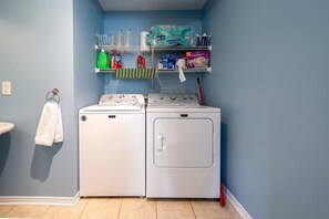 Een wasruimte met een wasmachine en droger, een plank met schoonmaakmiddelen en een handdoekrek.