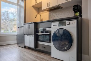 Cocina funcional con lavadora y secadora integradas, horno pequeño y ventana con vistas al exterior.