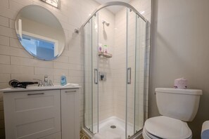 Un baño con ducha envuelta en vidrio, un inodoro blanco, un espejo redondo y un lavabo con dispensador de jabón.