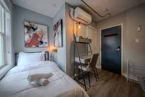 Ein Schlafzimmer mit Bett, Schreibtisch, Stuhl, Klimaanlage und Wandbild.