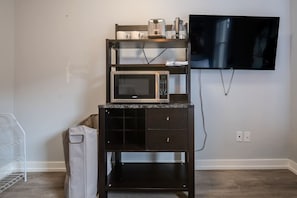 Eine Küchenzeile mit Mikrowelle, Toaster und Kaffeemaschine auf einem Regal, einem an der Wand montierten Fernseher und einem Mülleimer.