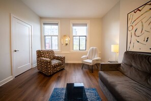 Een woonkamer met een gestreept fauteuil, een witte fauteuil, een bruine bank, een zwarte salontafel en een vloerkleed.