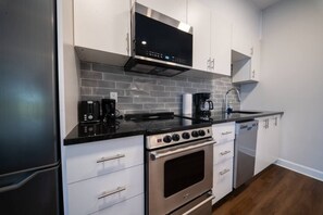 Une cuisine compacte équipée d’une cuisinière en acier inoxydable, d’un four à micro-ondes et d’une machine à café.