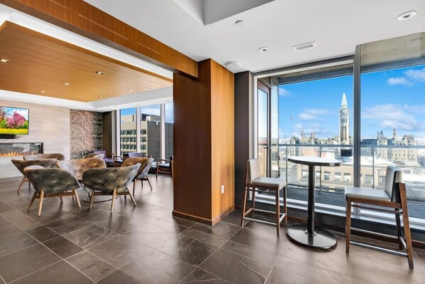 A modern hotel room with a large window offering a city view, a fireplace, and contemporary furniture.