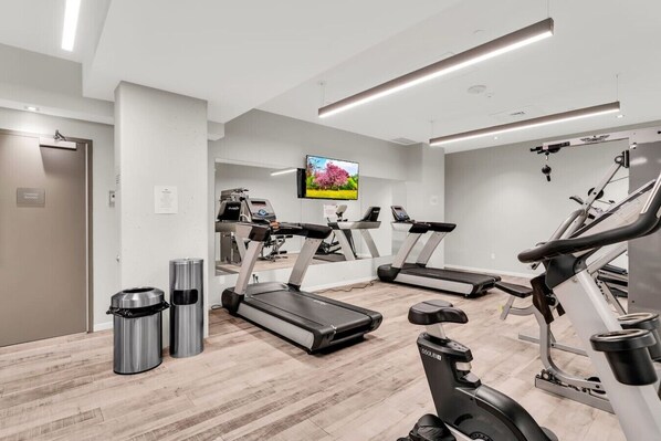 A gym with treadmills, stationary bikes, and a television screen.