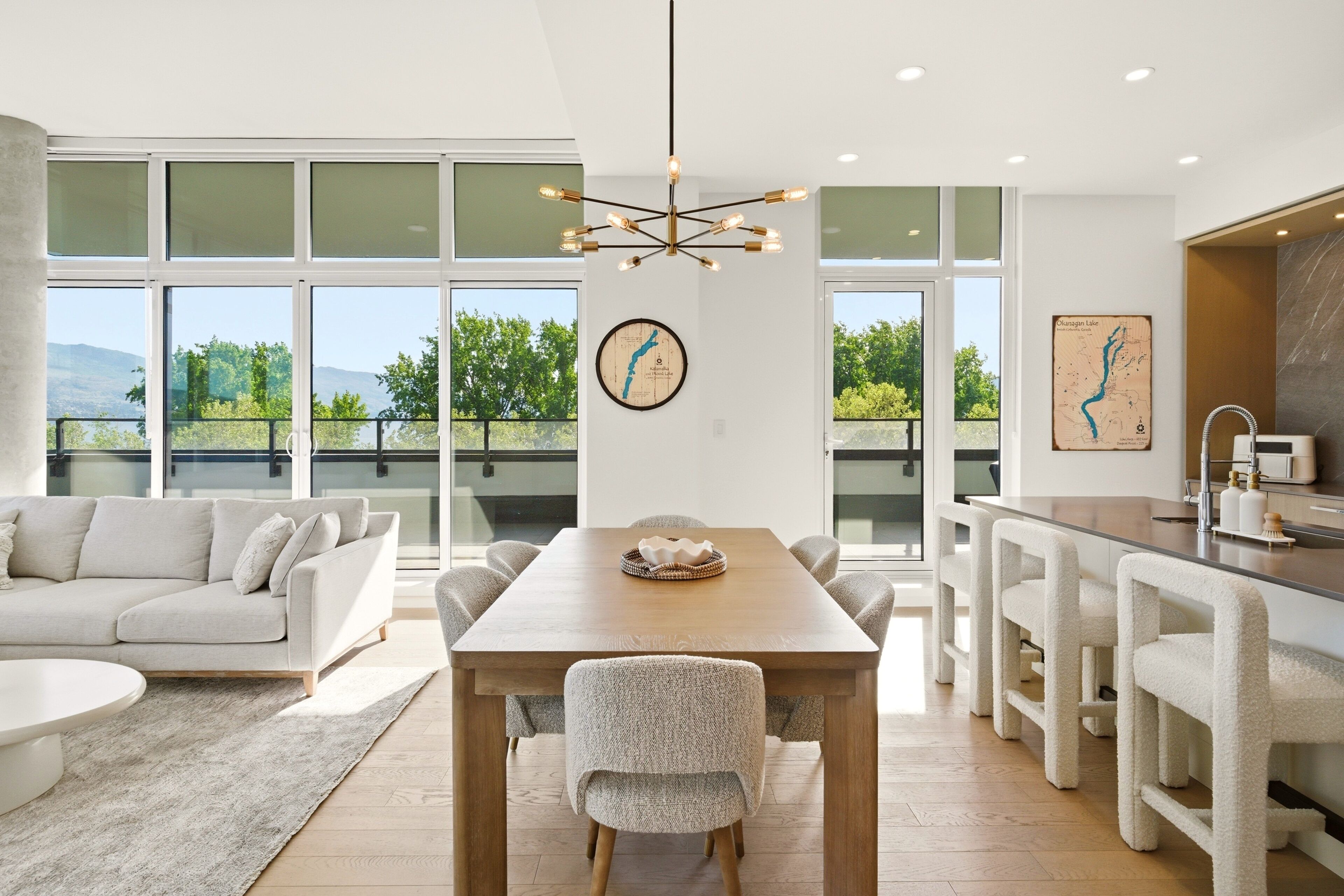 A modern interior with a dining area, kitchen, and large windows offering a view of greenery.