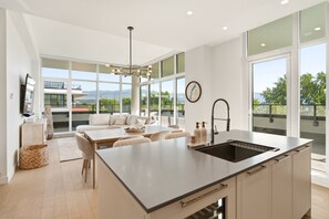 Una cocina moderna con una isla grande, un comedor con sofá y amplios ventanales que ofrecen vistas al exterior.