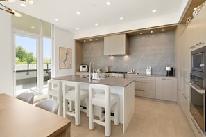 Una cocina moderna con una isla central, taburetes de bar, una mesa de comedor y vistas al exterior.