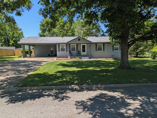 A single-story house with a covered porch, a lawn, and a large tree in front.