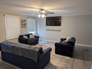 A living room with a ceiling fan, two dark sofas, a coffee table, and a mounted TV. - Bring the crew to this comfortable 3/2 home minutes from everything in Anniston (Anniston)