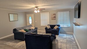 Ein Wohnzimmer mit zwei Sofas, einem Deckenventilator, einer Tür mit Buntglasfenster und einem an der Wand befestigten Fernseher.