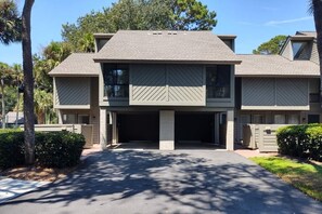 A two-story building with a garage, surrounded by trees and a well-maintained lawn. - Available 6/26-7/3/26 only! Sea Pines Villa; 2BR/2BA; Sleeps 6; HHI (Hilton Head Island)