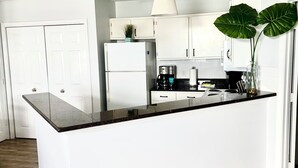 Une cuisine moderne avec des meubles blancs, un plan de travail noir et une grande plante verte.