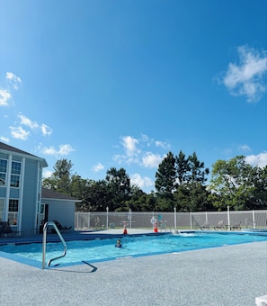 Una piscina con una scala in metallo, lettini da relax e una recinzione bianca.