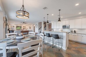 A spacious kitchen with white cabinets, a central island with bar stools, and a dining area with a round table and chairs. - GOLF View, Game Room, ALL King Beds, Htd Pool, Spa, Outdoor Kitchen, Putting Green, Corn Hole (Mesa)