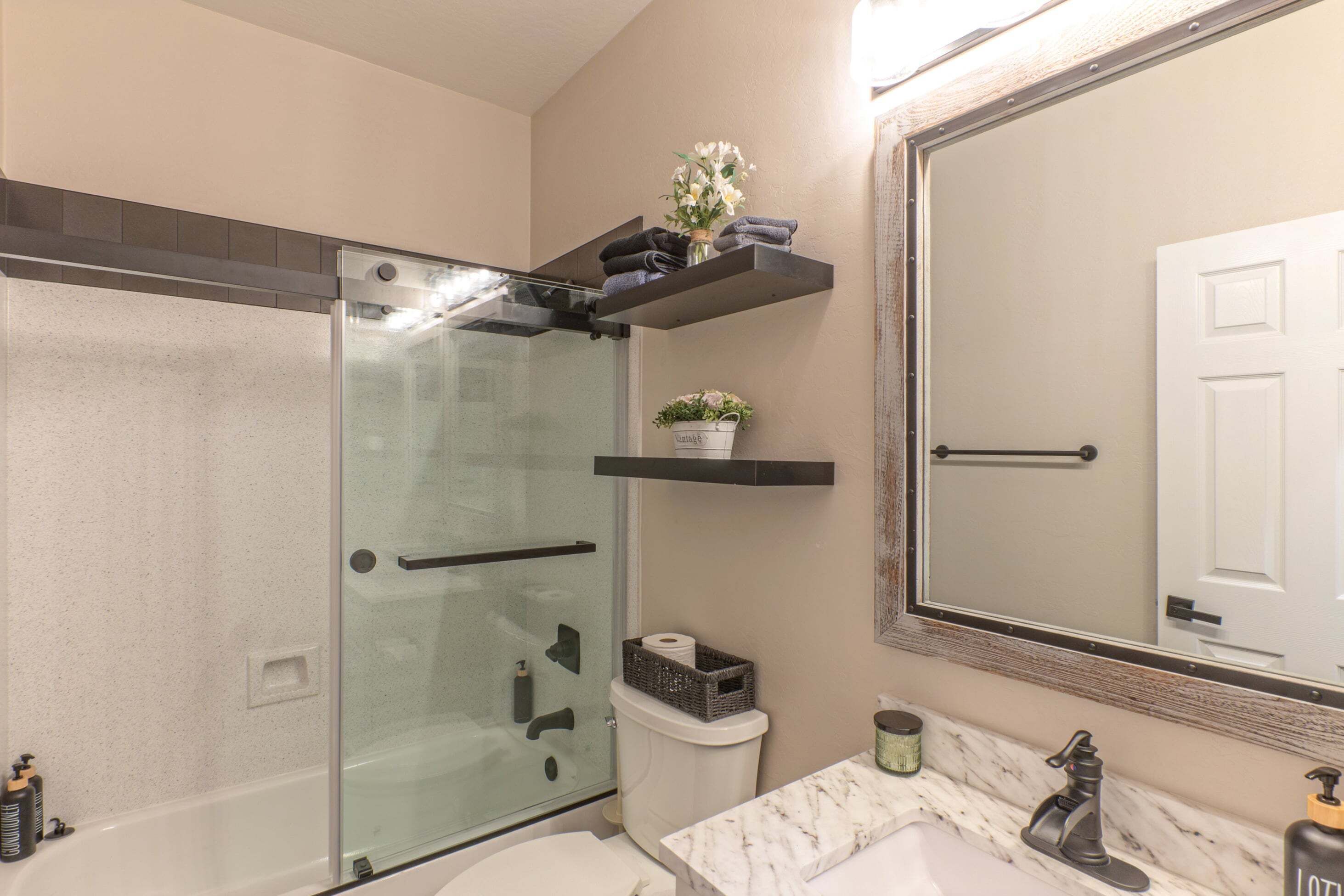 Une salle de bain avec une douche à parois de verre, des toilettes blanches, un lavabo en marbre et un miroir avec un cadre en bois.