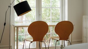 Ett rum med ett vitt skrivbord, två trästolar, en svart lampa och ett fönster med utsikt över grönområden.