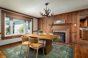 A dining area with a wooden table and chairs, a fireplace, and a chandelier. - Heritage House - 13m to Shenandoah NP, Pool, Hot Tub, Mountain Views, EV (Page County)