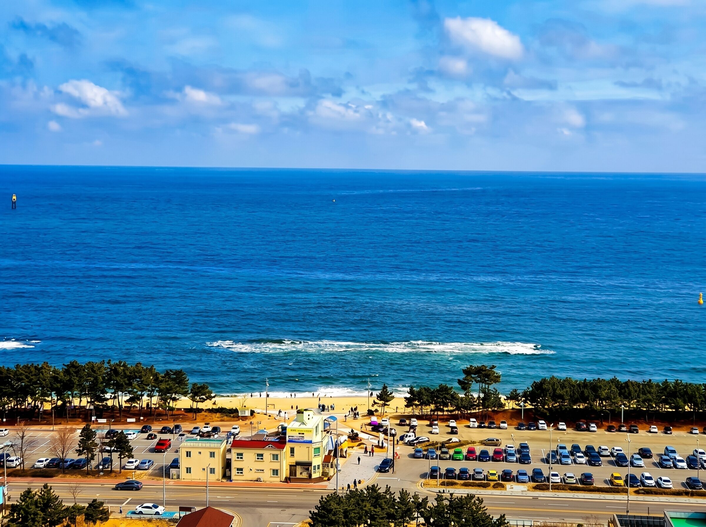 Un pueblo costero con playa, zona de estacionamiento y edificios a lo largo de la orilla.