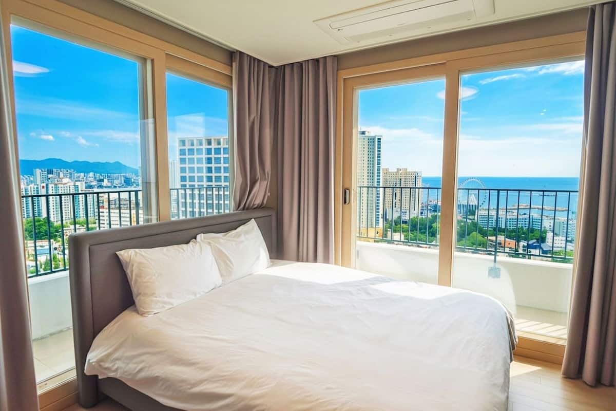 Una habitación de hotel con una cama grande, vistas de la ciudad y un balcón con barandilla.