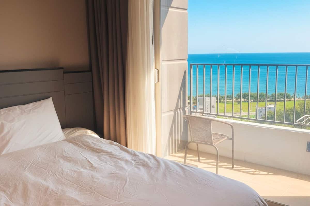 Una habitación de hotel con una cama, una silla y un balcón con vistas al océano.