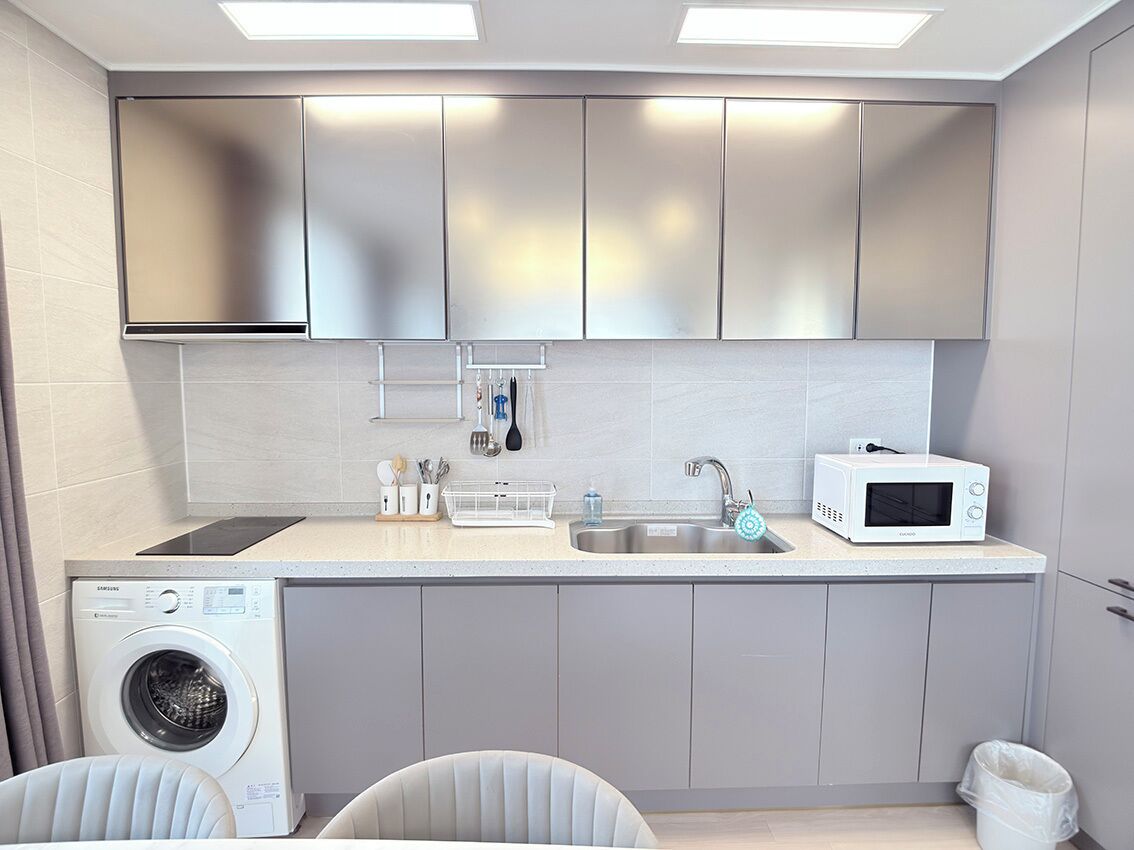 Una cocina compacta con lavadora, microondas y muebles de cocina modernos.
