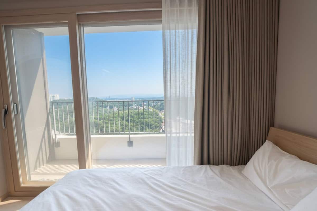Una habitación de hotel con una cama, vistas al balcón a través de una puerta corredera y una ventana con cortinas.