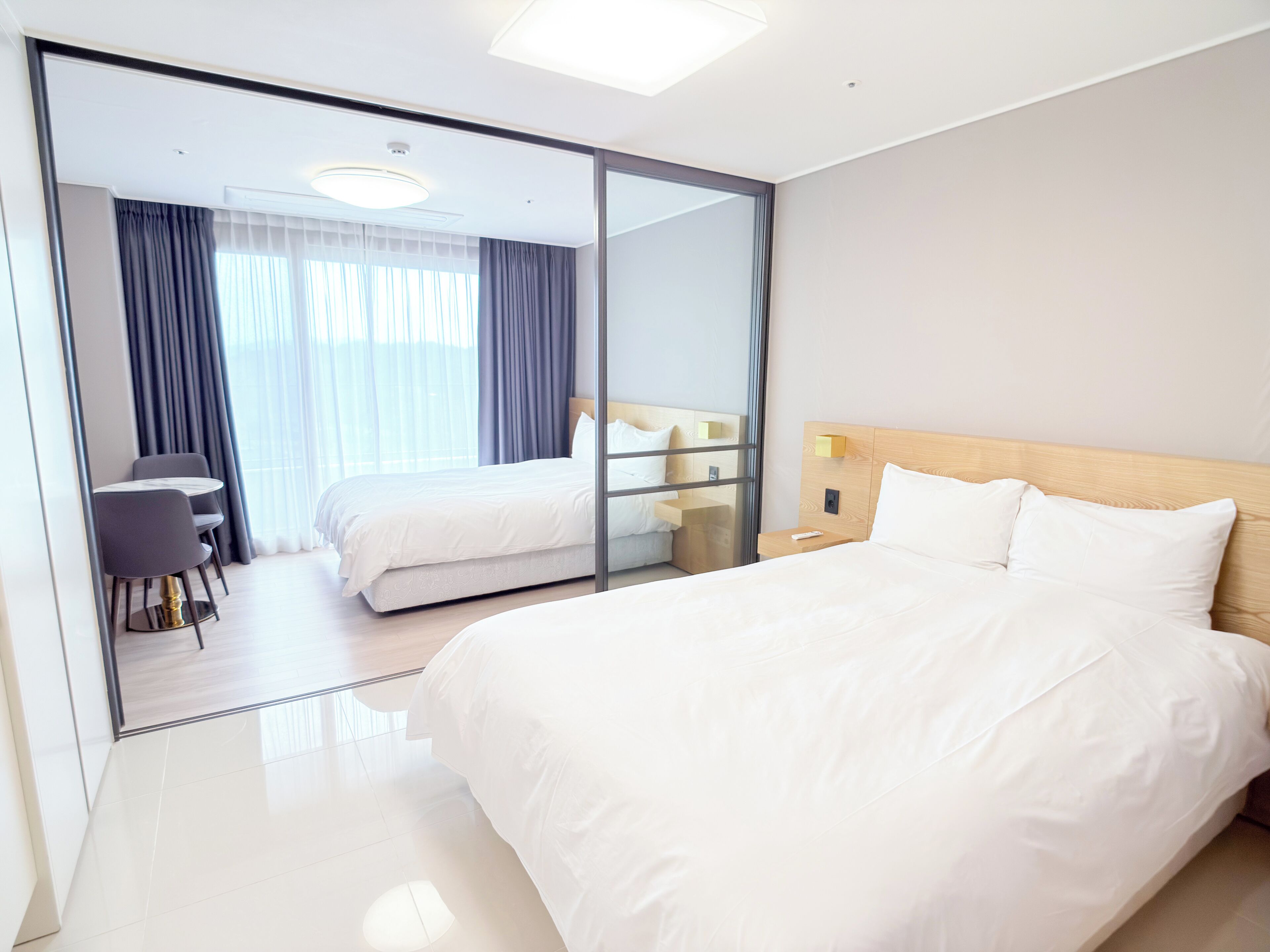 A modern hotel room with a large bed, a desk, and a glass partition.