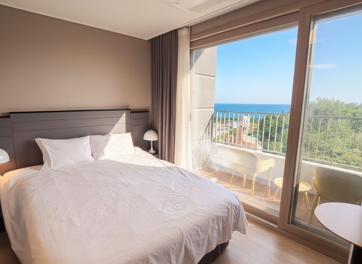 A hotel room with a large bed, a balcony with a view of the sea, and a small table and chairs.