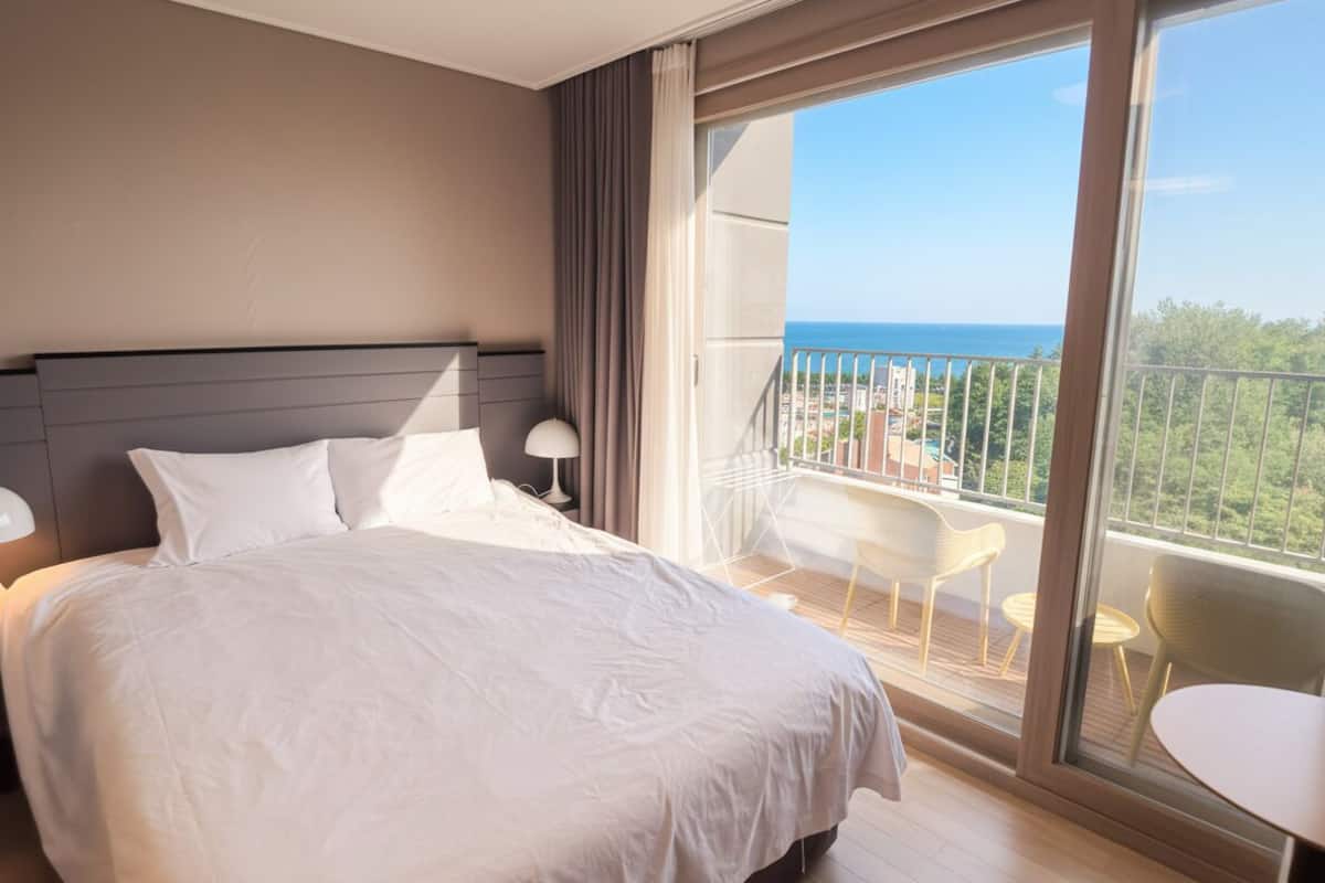 Una habitación de hotel con una cama grande, un balcón con vistas al mar y una pequeña mesa con sillas.