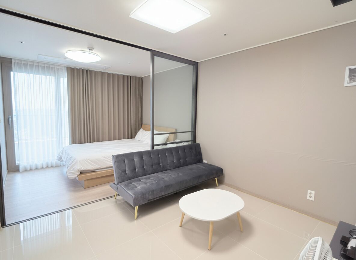 A modern hotel room with a bed, a sofa, a small table, and a mirror.