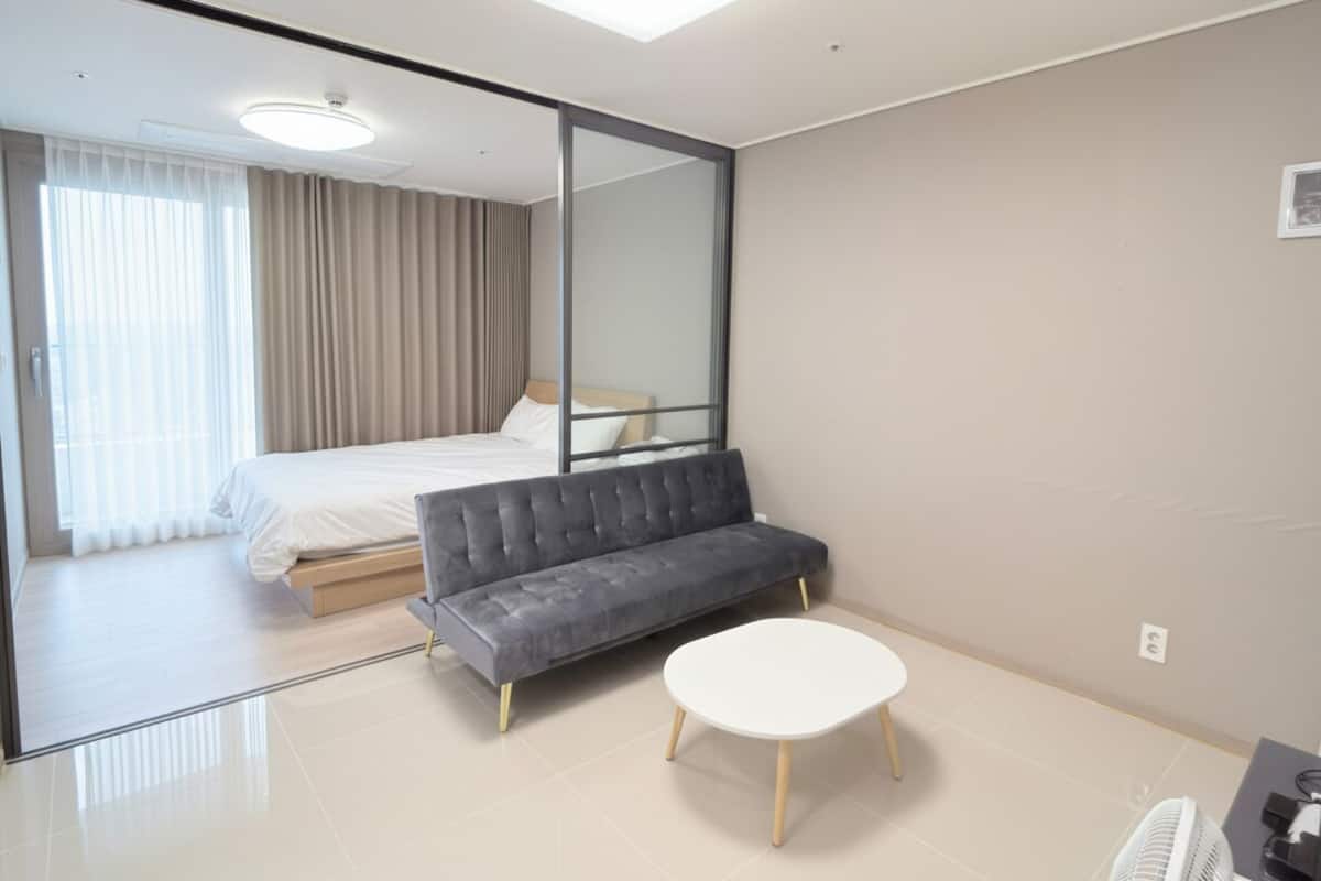 Una habitación de hotel moderna con una cama, un sofá, una mesita y un espejo.