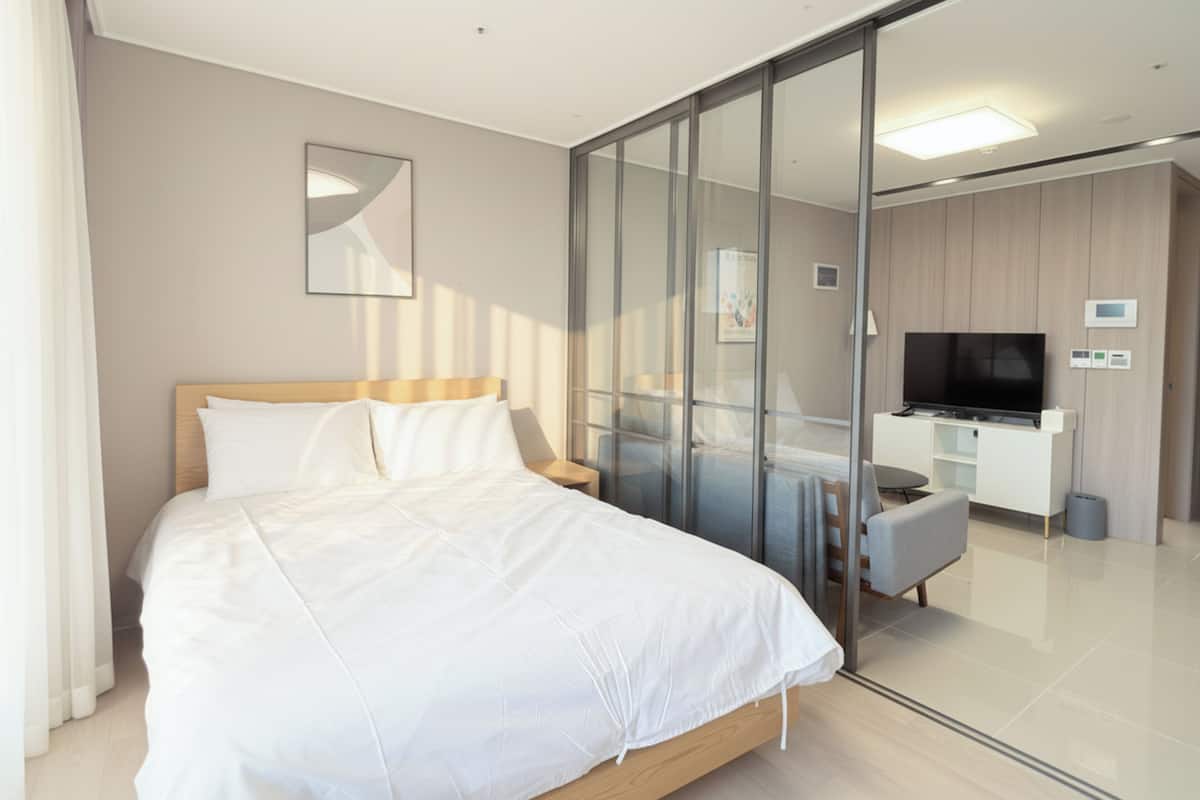 Una habitación de hotel moderna con una cama, un televisor, un escritorio y un panel de vidrio.