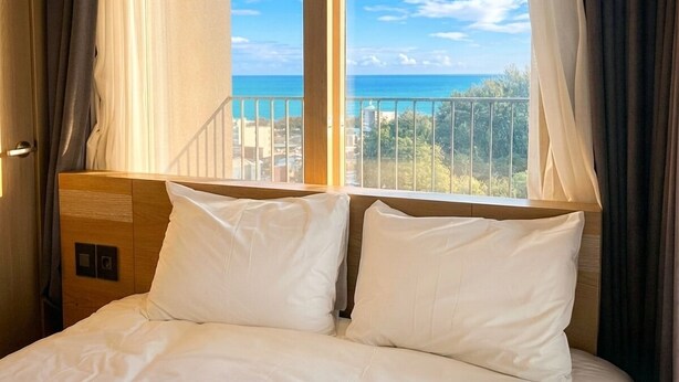 A hotel room with a bed, curtains, and a view of the sea. - Whalezip The Bluetera Ocean Stay (Sokcho)
