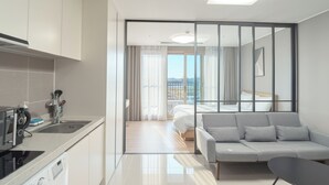 Ein modernes Hotelzimmer mit Küchenzeile, einer Couch, einem Bett und Blick ins Freie.