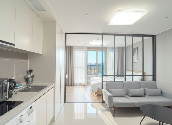 A modern hotel room with a kitchenette, a sofa, a bed, and a view of the outdoors.