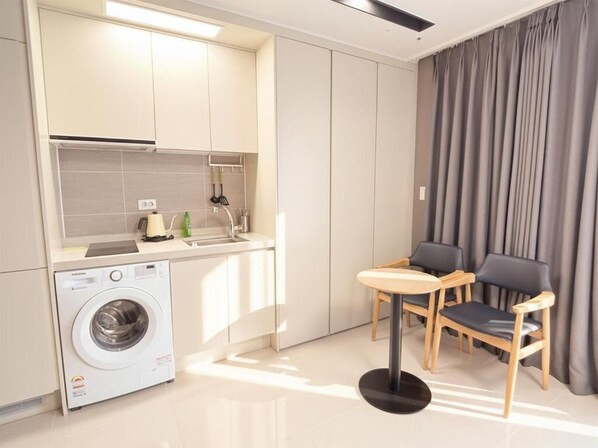 A compact kitchen with a washing machine, a small dining area with a table and chairs, and a large window with curtains.