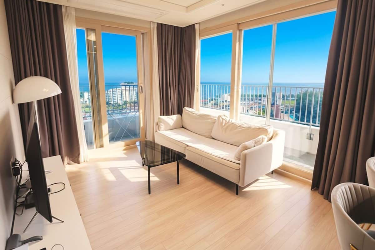 Una sala de estar moderna con un sofá, una mesa de centro, un televisor y ventanas amplias con vistas a la ciudad.