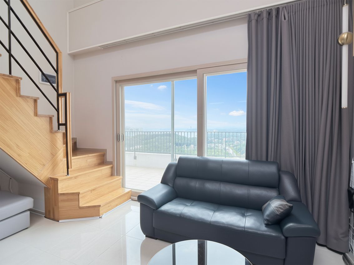 A modern living room with a leather sofa, a glass coffee table, a wooden staircase, and a large sliding glass door leading to a balcony with a city view.
