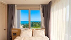 Ein Hotelzimmer mit Bett, Vorhängen, einem Fenster mit Meerblick und einer Tür.