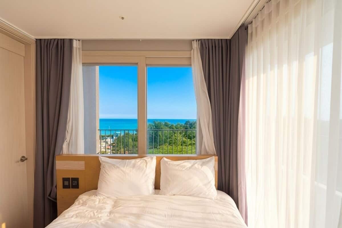 Habitación de hotel con cama, cortinas, ventana con vista al mar y puerta.