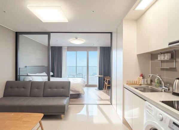 Una habitación de hotel moderna con sofá, cama, balcón, zona de cocina y lavadora.