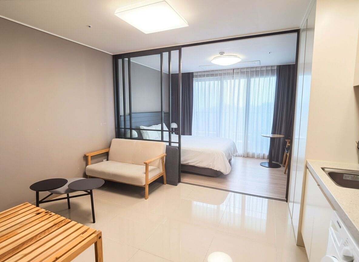 A hotel room with a bed, a sofa, a small table, a mirror, and a kitchen area.