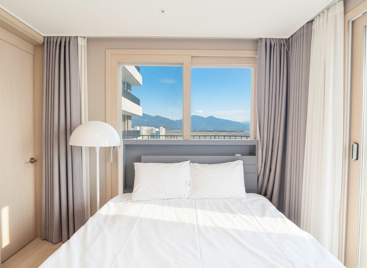 A hotel room with a bed, a lamp, and a window with curtains.